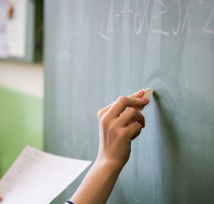 Young female teacher or a student writing math formula on blackboard in classroom.